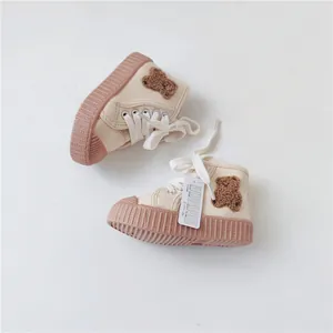 Detail view of beige baby canvas shoes featuring plush teddy bear patches and soft rubber soles