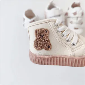 Close-up of cute brown 3D bear embroidery on beige toddler high-top canvas sneakers