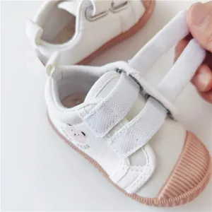Detail view of white canvas baby shoes with pink bear print and velcro straps.