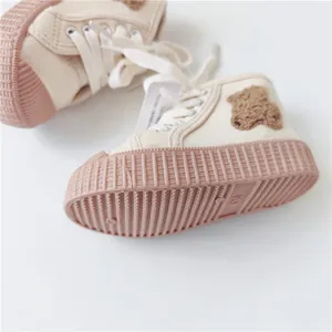 Detailed close-up of soft-sole children's canvas sneakers with a plush bear patch