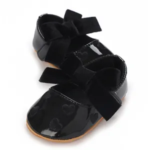 Dettaglio di scarpe neonata in vernice nera con fiocco in velluto e cuoricini