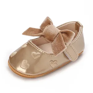 Primo piano di scarpa dorata da principessa per neonata con fiocco e ricami a cuore.