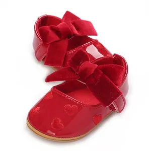 Dettaglio delle scarpe rosse per neonata con fiocco in velluto e cuori ricamati a mano