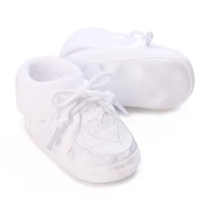 Close-up detail of white satin baby baptism shoe featuring soft sole and heart embroidery