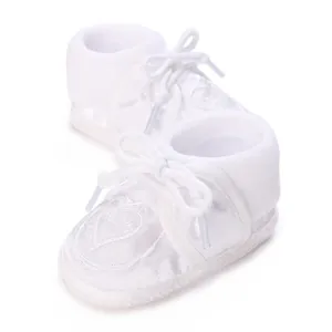 Macro detail of white infant christening shoes featuring elegant heart embroidery and soft soles