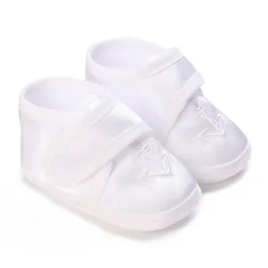 Detail shot of white soft-sole baby baptism shoes with an elegant embroidered anchor design.
