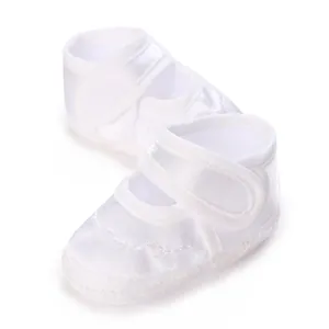 Nahaufnahme von weißen Satin-Babytaufschuhen mit weichen Sohlen und Klettverschluss