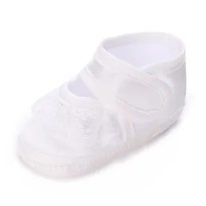 Détail d'une chaussure de baptême blanche en satin pour bébé avec dentelle et velcro