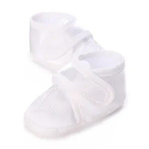 Close-up of white satin baby christening shoes with anchor embroidery and velcro strap