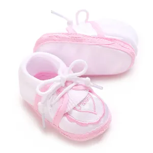 Close-up of cute pink and white baby soft-sole shoes with heart embroidery and laces