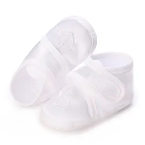 Vue détaillée de chaussures de baptême blanches pour bébé avec broderie ancre.