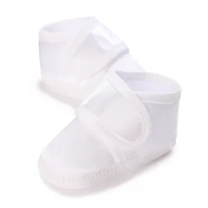 Close-up of white satin baby baptism shoes with soft soles and hook-loop strap