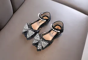 Detalle de zapatos de princesa para niña con gran lazo de pedrería y elegantes tiras de perlas