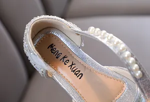 Primer plano de zapatos de princesa con purpurina plateada para niña y correa de perlas