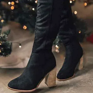 Close-up detail of black faux suede chunky high heel knee-high boots in warm light