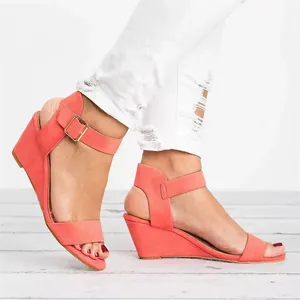 Detail of coral wedge sandals for women with adjustable ankle strap and gold buckle.