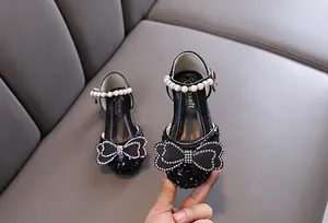 Close-up of girls' black princess shoes featuring pearl strap and rhinestone bow decoration