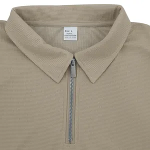 Dettaglio di una polo in maglia waffle kaki con colletto a mezza zip e etichetta taglia