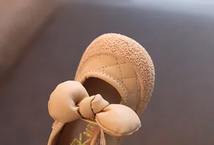 Détail d'une chaussure de marche beige pour bébé fille avec un grand nœud et un motif matelassé
