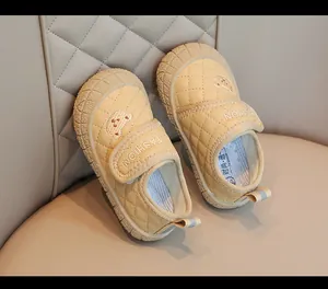 Dettaglio di scarpe gialle trapuntate per neonati con ricamo a orsetto e cinturino.
