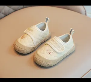 Primo piano di scarpe trapuntate per neonati color crema con ricamo orsetto e velcro