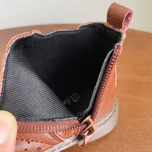 Primer plano de la cremallera lateral y el forro negro de estos botines marrones para niños pequeños.