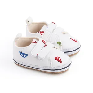 Détail de chaussures de marche pour bébé blanches avec motifs de voitures et bandes velcro.