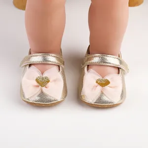 Nahaufnahme goldener Babyschuhe für Mädchen mit rosa Netzschleifen und glitzernden Herzen