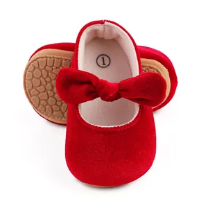 Close-up of red velvet baby shoes with a prominent bow and textured rubber sole