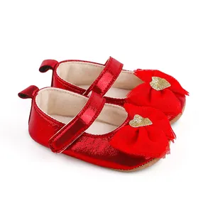 Close-up of red metallic baby girl shoes featuring a large mesh bow and gold heart.
