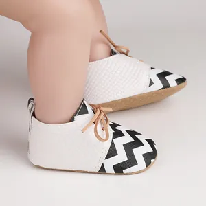 Close-up of baby walking shoes with black and white zigzag pattern and faux crocodile texture.