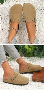 Close-up view of tan suede clogs with buckle strap and cork sole on white pebbles