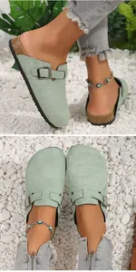 Close-up detail of sage green suede clogs with buckle strap on white pebble background
