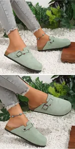 Light green suede closed-toe mules with cork sole and buckle detail shown on feet