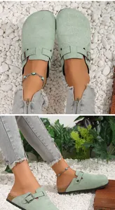 Close-up of mint green suede clogs with buckle detail and cork sole on white stones