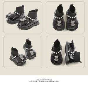 Detalle de zapatos de bebé negros estilo princesa con perlas y adorno de osito.