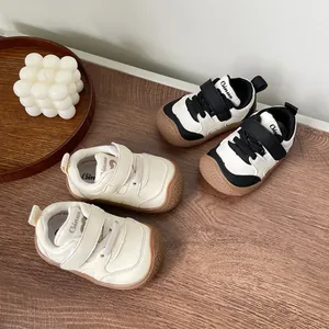Top view of baby toddler walking shoes in cream and black-white colors on wooden surface.