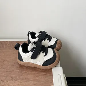 Black and white toddler sneakers with soft brown rubber soles and hook-and-loop straps.