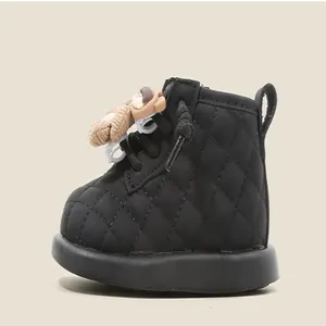 Détail de bottines noires matelassées pour bébé avec ornement en forme d'ours.