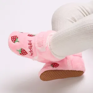 Close-up of pink plush baby booties with strawberry embroidery on an infant's foot