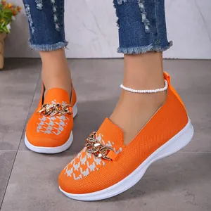 Détail de chaussures à enfiler en tricot orange avec chaîne dorée et semelle blanche.