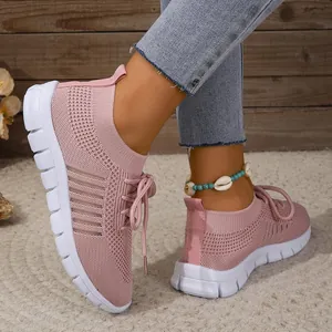 Close-up of pink breathable fly-knit sneakers on feet with white soles and laces