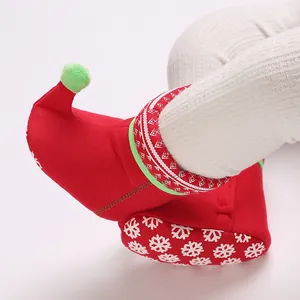 Close-up of red baby Christmas snow bootie with green pom-pom and snowflake sole