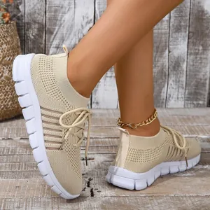 Detail view of beige breathable fly-knit lace-up sneakers on model with wood background
