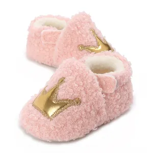 Macro view of pink fluffy baby warm shoes featuring a decorative gold crown patch detail.