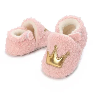 Close-up detail of soft pink fuzzy baby shoes featuring a gold crown embroidery patch