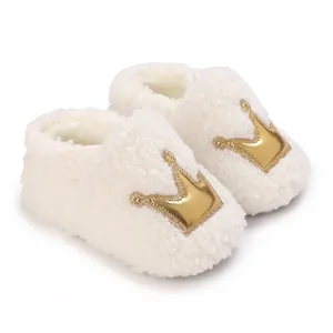 Close-up of soft white fleece baby booties featuring a shiny golden crown applique detail