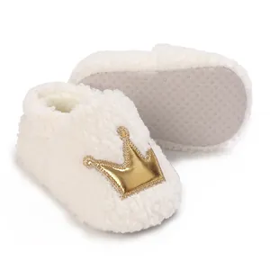 Detail view of white fuzzy baby shoes featuring a gold crown and anti-slip soft sole.