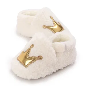 Detailed view of soft white sherpa baby shoes with a shiny gold crown patch for infants