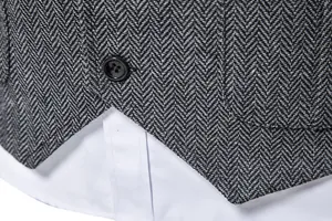 Dettaglio del gilet in tweed grigio spigato con bottone nero e camicia bianca sotto